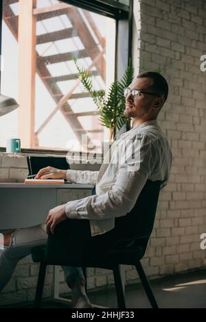 Thoughtful man holding pen and looking away while sitting at his working place in office. Using tablet. Stock Photo