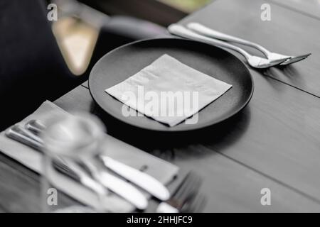 Black plate, cutlery and napkin on wooden table view Table setting in a restaurant. Stock Photo