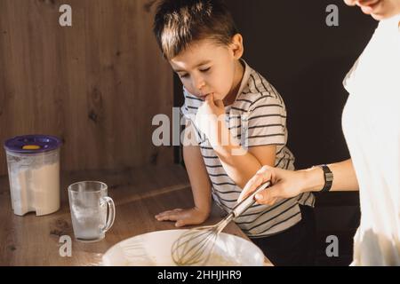 Mother's hands mixing ingredients for dough with son at modern kitchen. Parent helping child. Family weekend. Stock Photo