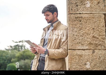 From below joyful young Asian male with dark hair in casual outfit and earphones while having video call on laptop on city street Stock Photo