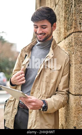 Cheerful male student in formal wear standing with laptop case and browsing digital tablet on street Stock Photo
