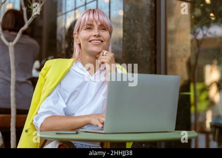 Joyful woman working on laptop at outdoor cafe Stock Photo