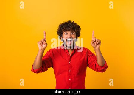 Attractive bearded man with astonished shocked facial expression pointing up with both fingers, presenting copy space. Indoor studio shot isolated on orange background Stock Photo