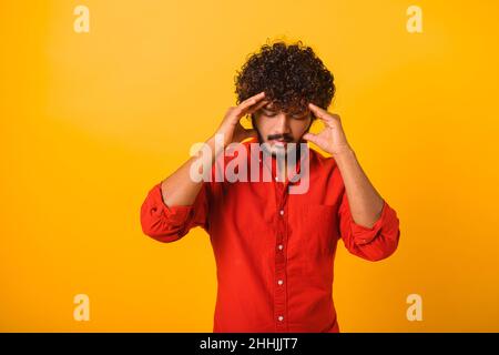 Depressed man rubbing head, feeling sad because of hopelessness and loneliness, nervous breakdown. Indoor studio shot isolated on orange background Stock Photo