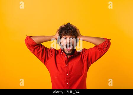 Excited shocked man holding hands on face and screaming looking at camera with big eyes and open mouth, shocked bemused with news, win at lottery. Indoor studio shot isolated on orange background Stock Photo