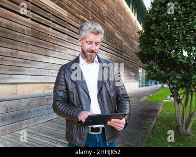 Content male surfing internet on modern black tablet while standing near wooden building in city Stock Photo