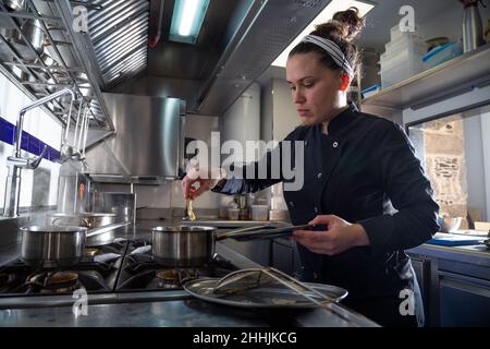 Woman in dark uniform putting shrimp into saucepan with hot oil while working in kitchen of modern restaurant Stock Photo