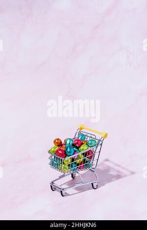 A shopping cart with colourful chocolate eggs on a pink background. Stock Photo