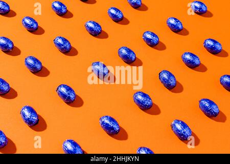 Pattern of blue foil chocolate eggs on a orange background. Stock Photo