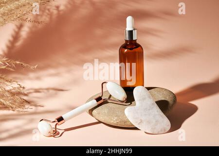 Gua Sha massage tools and essential oil on a river pebble stone on a beige background. Home skin care anti-aging and beauty concept. Stock Photo