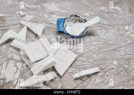 Home, interior reconstruction still life. Broken gypsum pieces of decorative stucco cornices. Bowl with white plaster and trowel. Dirty plastic ground Stock Photo