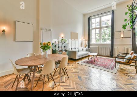 Light living room decorated with green plants furnished with comfortable couch and wooden table and armchairs placed near window Stock Photo