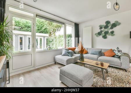 Comfortable corner sofa with cushions and pouf in stylish spacious studio apartment with windows and door giving access to a beautiful garden Stock Photo