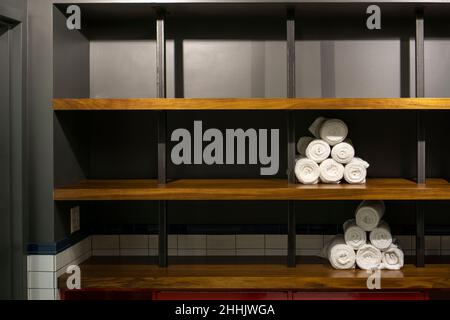 Rolled white gym towels in a bathroom on wooden shelves. Piled towels among empty spaces Stock Photo