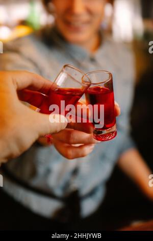 Soft focus of crop unrecognizable female barkeeper clinking with alcoholic red blood shots with faceless person while working in bar Stock Photo