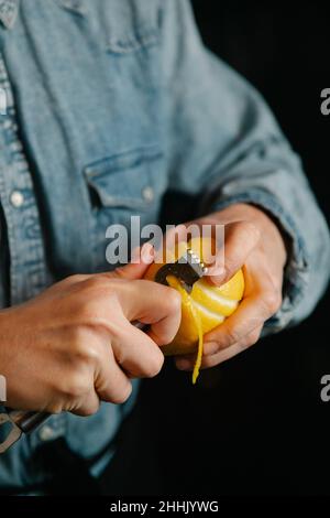 Cropped unrecognizable female bartender taking off lemon zest while preparing for making cocktail in bar during work Stock Photo