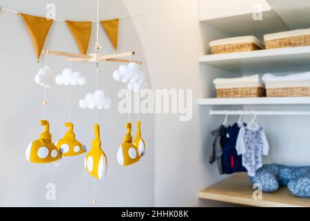 Baby crib mobile with various soft similar toy submarines in light kids bedroom with reflection on white wall at home near wardrobe Stock Photo