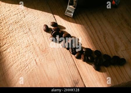 High angle of fresh roasted coffee beans placed on rough wooden table with scratches in kitchen in sunlight Stock Photo