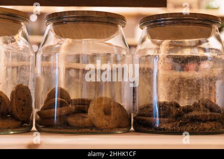 Set of glass jars with chocolate cookies placed on wooden shelf in shop Stock Photo
