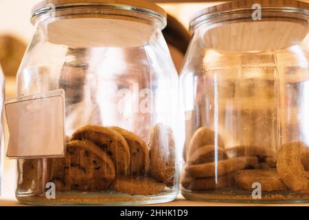 Set of glass jars with chocolate cookies placed on wooden shelf in shop Stock Photo