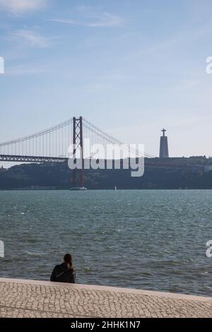 25 April Bridge and one person sitted by Tejo River at Lisbon Stock Photo