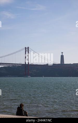 25 April Bridge and one person sitted by Tejo River at Lisbon Stock Photo