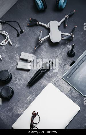 Top view of modern appliances for UAV drone including charger batteries and tripod near netbook and graphics tablet on gray desk Stock Photo