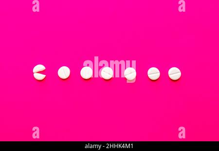 From above of broken and whole circle shaped pills placed in even line on vivid pink background in studio Stock Photo