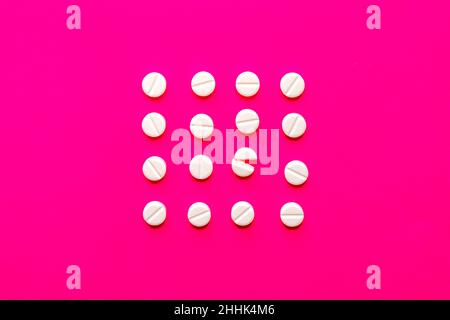 Top view of white circle shaped whole pills and broken pill placed in rows on bright pink background in studio Stock Photo