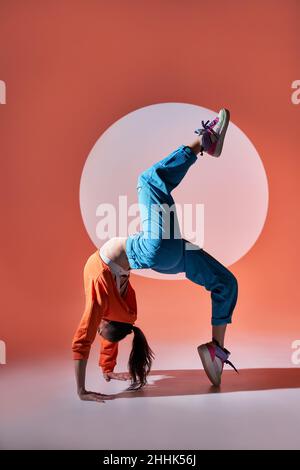Full body side view of active female dancer performing graceful wheel pose and raising leg while dancing in studio with circle on wall Stock Photo