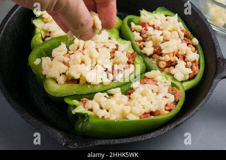 Crop anonymous person adding cheese on green bell peppers with pizza stuffing in frying pan during cooking process in kitchen Stock Photo