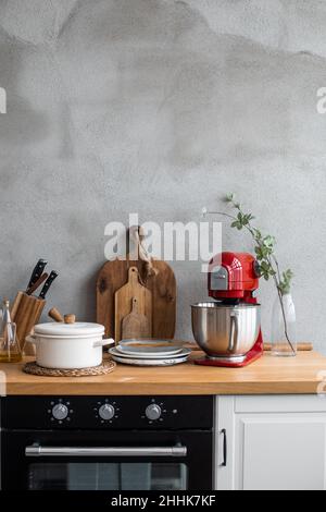 Wooden counter with set of kitchenware near set of cutting boards and knives near modern hand mixer in light kitchen Stock Photo