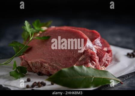 From above of fresh uncooked beef fillet with green parsley placed on slate board with parchment paper in kitchen Stock Photo