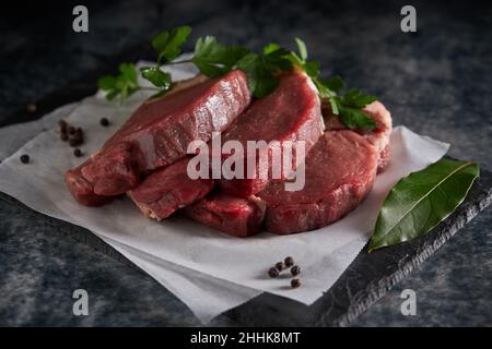 From above of fresh uncooked beef fillet with green parsley placed on slate board with parchment paper in kitchen Stock Photo