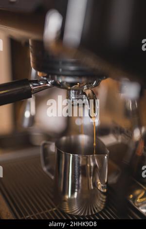 Freshly brewed espresso pouring from portafiller in professional coffee machine into stainless milk pitcher Stock Photo