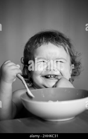 Smiling baby eating food. Launching child with spoon. Stock Photo