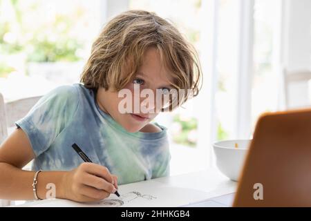 Boy (8-9) drawing picture during online lesson Stock Photo