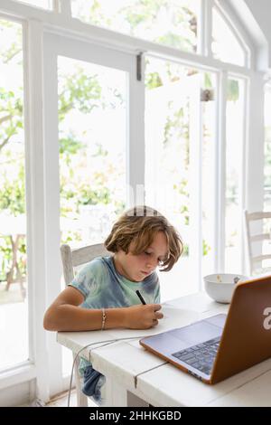 Boy (8-9) drawing picture during online lesson Stock Photo