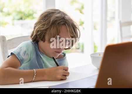 Boy (8-9) drawing picture during online lesson Stock Photo