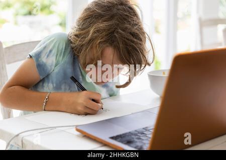 Boy (8-9) drawing picture during online lesson Stock Photo