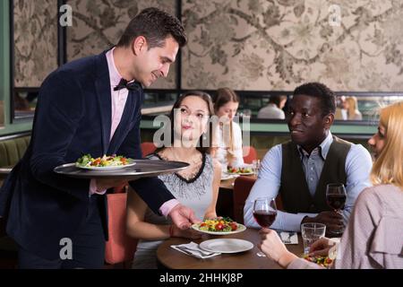 Polite waiter bringing dishes to guests Stock Photo