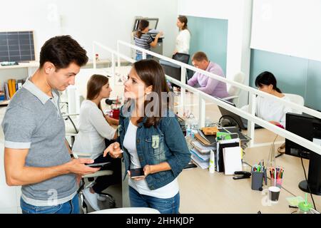 Friendly male and female colleagues exchanging phone numbers in modern coworking space Stock Photo