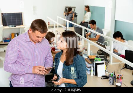 Friendly male and female colleagues exchanging phone numbers in modern coworking space Stock Photo
