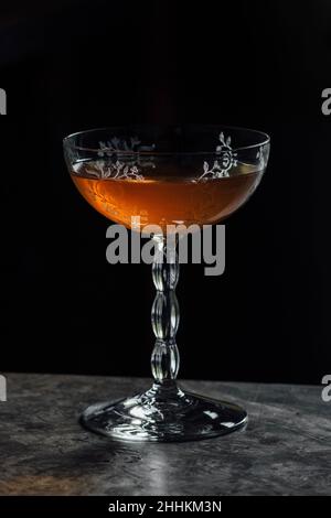 amber colored Emerson cocktail in vintage etched glassware Stock Photo