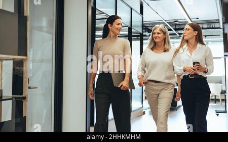 Three cheerful businesswomen walking together in an office. Diverse group of businesswomen smiling while having a discussion. Successful female collea Stock Photo