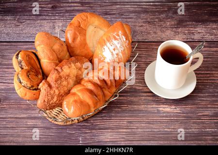 Assortment of fresh homemade pastries and a cup of hot black tea on a wooden table. Top view, flat lay. Stock Photo