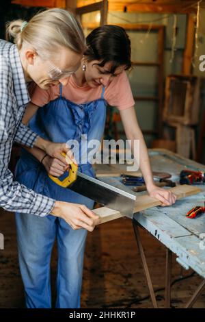 Man teaching Woman to working with wood in workshop. Sewing wood. Reuse, reduce, recycle old things. Aware consumption and gender equality. Tools to Stock Photo