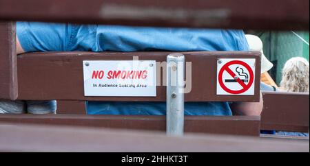 Closeup of a NO SMOKING sign on the back of a wooden bench at an outdoor concert venue. Stock Photo