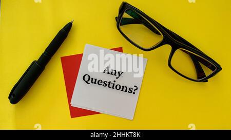 Any questions text on white notepad with pen, glasses and alarm clock on yellow cover table. Business concept. Stock Photo
