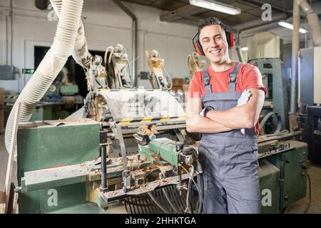 Cheerful male carpenter in uniform standing in professional joinery Stock Photo